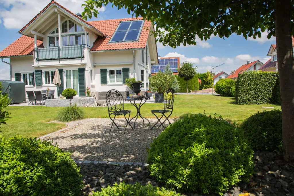 Gestalteter Garten mit Rasen, Sitzplatz und Bäumen vor einem Wohnhaus